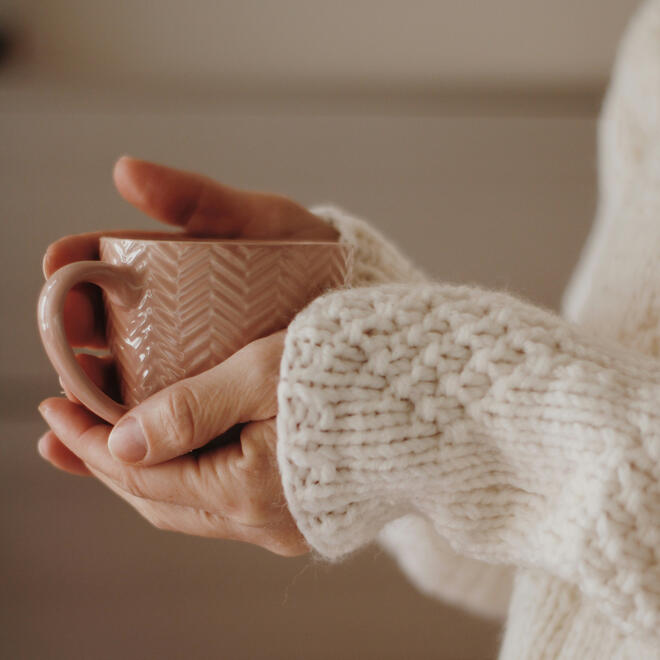 A woman wearing a soft sweater cradles a warm cup, exuding a sense of relaxation and contentment.